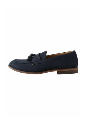 Mocasines de ante azul marino con punta redondeada, borlas decorativas y suela marrón en contraste. Textura suave y detalles de costura mínimos.