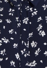 Marineblouse met een klein wit bloemmotief, kraag, knoopsluiting en zachte stoftextuur. Bevat een voorflap en korte mouwen.