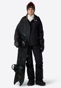 Černá snowboardová bunda přes bílou střední vrstvu, černé snowboardové kalhoty, rukavice a černý snowboard se vázáním a příslušenstvím. Brýle s červeným zabarvením.