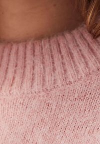 Light pink sweater featuring a ribbed neckline and soft, textured fabric, showcasing a cozy, knitted pattern along the body.