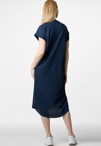 Marineblaues Kleid mit kurzen Ärmeln, knielang, lässiger Schnitt, seitlichen Schlitzen und glattem Stoff. Getragen mit weißen Sneakers.