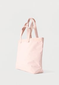 Svetloružová obdĺžniková taška na rameno s dvoma rúčkami a jemne vyrazeným názvom značky na rúčkach na jednoduchom svetlom pozadí.