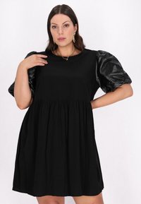 Rochie neagră cu un corset strâns și o fustă evazată. Mîneci bufante din material lucios. Textură netedă, design casual și lungime până la genunchi.