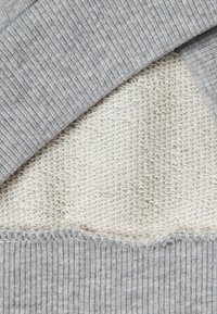 Šedý a krémový svetr s vrstveným pletením, s žebrovanou texturou v horní části a hladkým pleteným vzorem v dolní části.