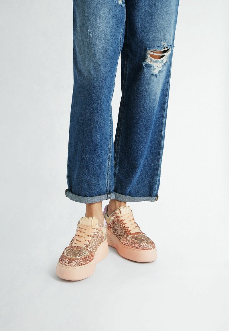 Jambes portant un jean bleu déchiré retroussé et des baskets compensées épaisses en rose et or rose pailleté.