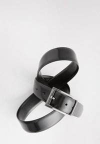 Czarny skórzany pasek o połyskującym wykończeniu z metalową, srebrną klamrą. Posiada perforacje wzdłuż paska umożliwiające regulację. Teksturowana wewnętrzna strona.