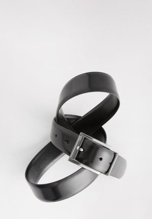 Juodas odinis diržas su blizgiu paviršiumi ir sidabro spalvos metaline sagtimi. Dirželyje yra perforacijos reguliavimui. Vidinė pusė tekstūruota.