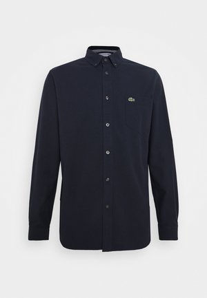 Marineblaues langärmliges Hemd mit Knopfleiste, geknöpftem Kragen, Brusttasche und kleinem grünem Krokodil-Logo auf der linken Seite.