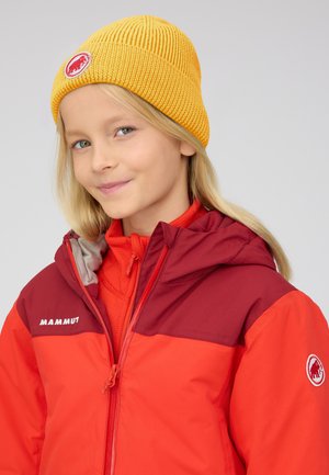 Young person wearing a yellow knit hat and a red Mammut jacket with a hood, smiling slightly against a neutral background.