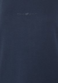 Dunkelblaues T-Shirt mit kurzen Ärmeln aus Baumwolle, mit einem dezenten, eingeprägten "POLO SYLT"-Logo auf der Vorderseite. Glatte Textur.