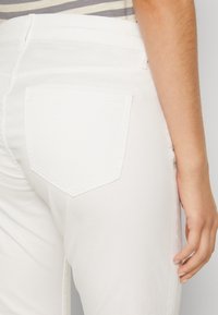 White denim jeans with a back pocket, featuring a curved top edge and subtle stitching details. The fabric appears smooth and thick.