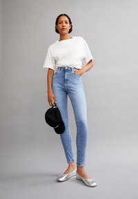 Una camiseta blanca de gran tamaño, jeans ajustados de talle alto en un tono azul claro, bailarinas plateadas y una gorra de béisbol negra en la mano.