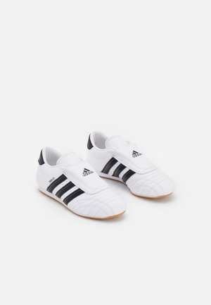 Weiße Adidas-Kleinkindschuhe mit schwarzen Streifen, Klettverschlüssen und hellbraunen Sohlen, nebeneinander auf einem weißen Hintergrund positioniert.