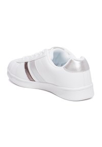 Zapatilla blanca con acentos metálicos plateados y dos rayas tonales. Material sintético suave, punta redonda y suela de goma texturizada.
