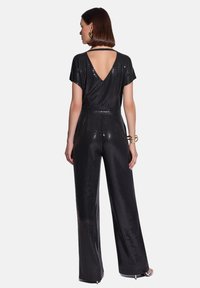 Czarny kombinezon z cekinami, z dekoltem w kształcie litery V na plecach, krótkimi rękawami, dopasowaną talią i szerokimi nogawkami, o gładkiej teksturze i błyszczącej powierzchni.