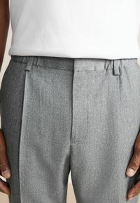 Gray wool trousers with a textured finish, featuring a flat front, belt loops, and neatly pressed creases. Accompanied by a white t-shirt.