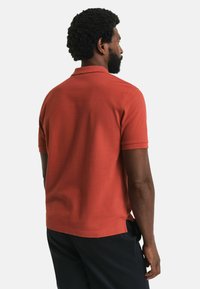 Kurzarm-Polohemd in rostorange mit strukturiertem Strickstoff, klassischem Kragen und Seitenschlitzen für Atmungsaktivität.