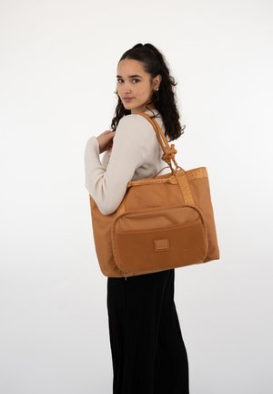 Tan tote bag made of nylon, featuring a structured shape, textured front pocket, adjustable top handle, and logo accent.