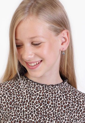Tijgerprint top met hoge halslijn. Het model draagt zilveren dangle oorbellen met een bloemmotief. Glad, steil blond haar.