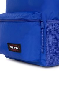 Modrá batoh vyrobený z odolné tkaniny, s přední kapsou na zip a síťovou boční kapsou. Výrazná černá nášivka loga na dolní části přední strany.