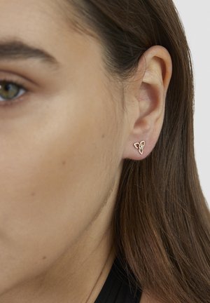Close-up of a woman's ear wearing a small gold triangular stud earring with a central stone and leaf-shaped details.