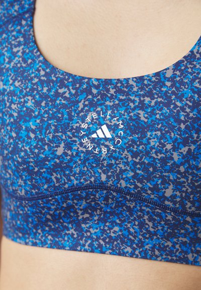 Sujeción deportiva en un patrón abstracto azul y gris. Presenta un escote redondo, costuras planas y un logo blanco central con un diseño de tres rayas.