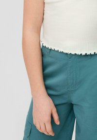Witte geribbelde cropped top met golvende zoom, gecombineerd met teal cargo broek met een zijzak en een soepele stofstructuur.