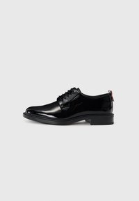 Chaussures en cuir verni noir avec une texture lisse, �à lacets, à bout rond et avec un petit talon empilé bas comportant un accent rouge à l'arrière.