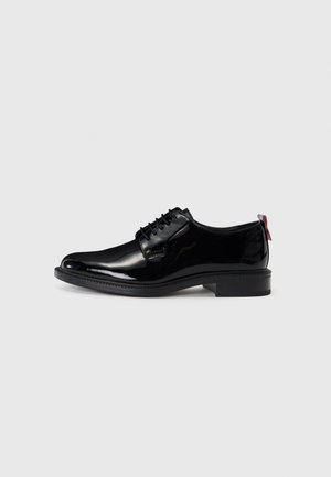 Black patent leather shoes with a smooth texture, lace-up design, round toe, and a low stacked heel featuring a small red accent at the back.
