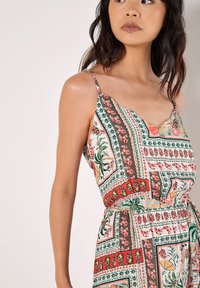 Farbiger gemusterter Jumpsuit mit dünnen Spaghetti-Trägern, der botanische und geometrische Designs in Rottönen, Grün und Creme zeigt.