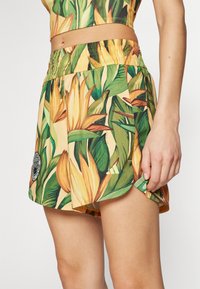 Shorts made of lightweight fabric with a yellow base and bold green leaves and orange flowers pattern. Elastic waistband and logo detail.
