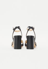 Zwarte hoge hakken sandalen met een chunky hak en kruislings strap ontwerp. Gemaakt van soepel leer met een beige binnenvoering en een enkelgesp sluiting.