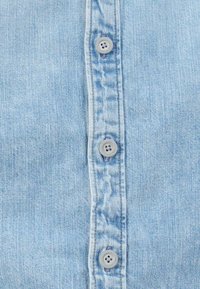  Lichtblauw denim overhemd met een voorste knoopsluiting en zes grijze knopen. De stof heeft een zachte, gestructureerde afwerking.