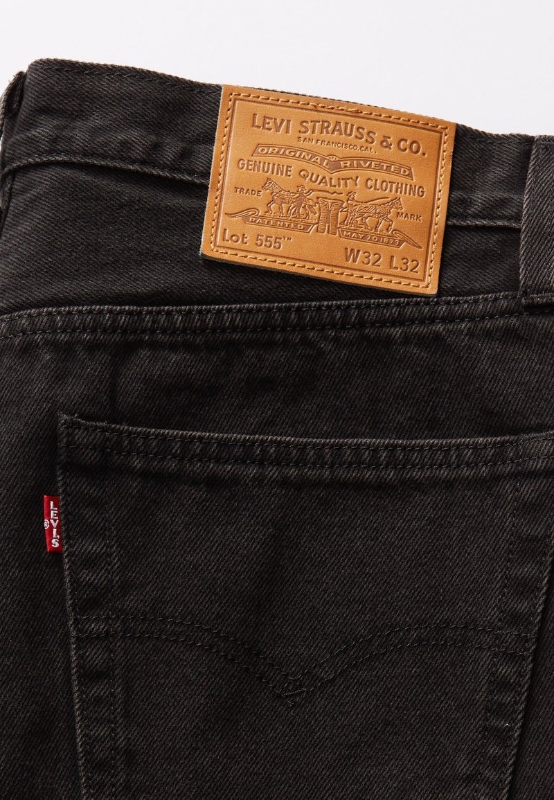 Zwarte denim jeans met een leren merkembleem, waarin het Levi's logo is verwerkt. Achterzak met een rood label en zichtbare stikseldetails.