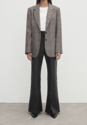 Kvinde iført en grå ternet blazer over en hvid top med højtaljede sorte flared bukser og sorte spidse sko.