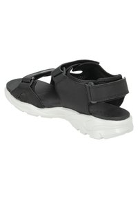 Svart sandal med ovandel i tyg, justerbara remmar, en texturerad innersula och en tjock vit gummisula för stöd.