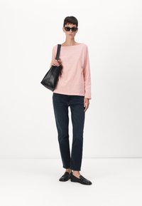 Camisa de manga larga color rosa claro con un escote amplio; vaqueros azul oscuro; bolso negro; zapatos negros sin cordones; gafas de sol rectangulares.