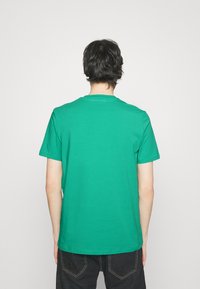 Grøn bomulds t-shirt med korte ærmer, rund halsudskæring og en glat tekstur, vist fra ryggen. Sorte denim bukser synlige nedenunder.