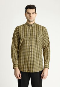 Camisa de manga larga con un patrón a cuadros en amarillo y negro, cierre frontal de botones, cuello clásico y puños con detalle de cuadros a juego.