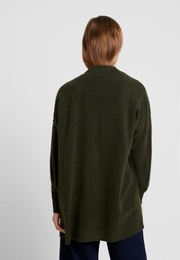 Knitted green sweater with a loose fit, long sleeves, and a ribbed hem, featuring a high neckline and soft texture. No visible patterns.