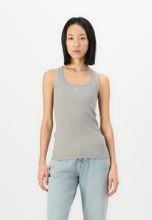 Light gray ribbed tank top with a round neckline and narrow straps, paired with light blue jeans. Subtle logo detail at the chest.