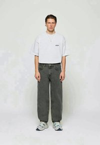 Λευκό oversized t-shirt με κοντά μανίκια, γκρι παντελόνι ψηλής μέσης και αθλητικά παπούτσια με μπλε λεπτομέρειες; απλός σχεδιασμός και χαλαρή εφαρμογή.