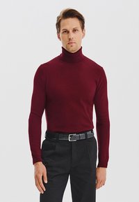 Burgundowa sweter z golfem, wykonany z miękkiego materiału, dopasowany krój, długie rękawy, w zestawie z czarnymi spodniami i czarnym paskiem.