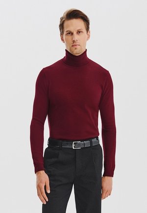 Burgundowa sweter z golfem, wykonany z miękkiego materiału, dopasowany krój, długie rękawy, w zestawie z czarnymi spodniami i czarnym paskiem.