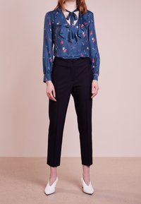 Bluzka w kwiatowy wzór w ciemnoniebieskim kolorze z falbaniastymi detalami i wiązaniem pod szyją, zestawiona z dopasowanymi czarnymi spodniami i białymi szpilkami.