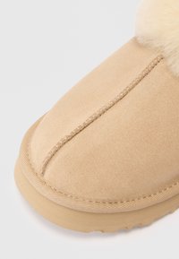 Beige suede støvlett med rund tå, med myk pelskant langs åpningen og detaljert søm langs sømmen. Teksturert gummisåle.