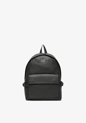Schwarzer Leder-Rucksack mit vorderer Reißverschlusstasche, oberem Griff und verstellbaren seitlichen Riemen vor weißem Hintergrund.