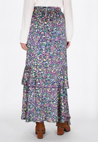 Többrétegű, színes maxi szoknya virágmintákkal, rugalmas derékrésszel, könnyű anyagból készült, barna, blokk sarkú csizmával viselve.