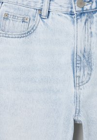 Détail avant d'un jean en denim bleu clair montrant la ceinture, le bouton, la zone de la fermeture éclair et les poches avant avec rivets.