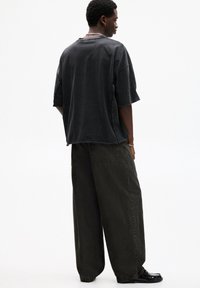 T-shirt nera in cotone di grandezza oversize con orlo grezzo e maniche corte, abbinata a pantaloni larghi color verde oliva scuro con tasche posteriori.